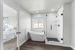 Ensuite bathroom featuring a freestanding tub, a shower stall, dark wood-type flooring, a textured ceiling, and tile walls