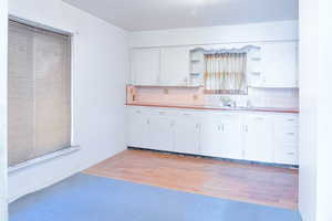 Kitchen featuring light countertops, white cabinets, open shelves, light wood-style flooring, and decorative backsplash