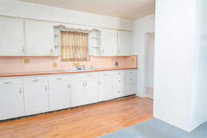 Kitchen featuring light countertops, white cabinets, open shelves, light wood-style flooring, and decorative backsplash