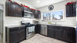 Kitchen featuring appliances with stainless steel finishes, light stone countertops, decorative backsplash, light tile patterned floors, and recessed lighting