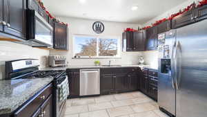 Kitchen featuring stainless steel appliances, tasteful backsplash, light stone counters, recessed lighting, and dark brown cabinets