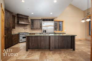Kitchen with dark brown cabinets, dark stone counters, an island with sink, decorative backsplash, and lofted ceiling