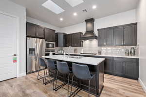 Kitchen with appliances with stainless steel finishes, a center island with sink, backsplash, a kitchen bar, and custom range hood
