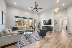 Living area with a towering ceiling, light wood-style flooring, ceiling fan, and recessed lighting