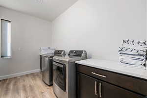 Washroom with light wood-style floors, independent washer and dryer, and cabinet space