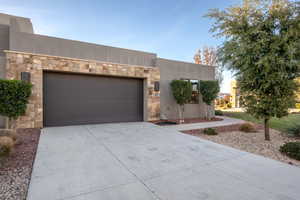 View of front of home with stone siding, driveway, a garage, and stucco siding