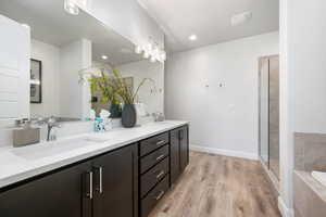 Bathroom with light wood-type flooring, double vanity, a stall shower, a relaxing tiled tub, and recessed lighting