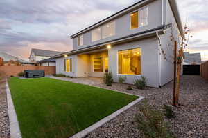 Back of property at dusk featuring a fenced backyard, stucco siding, a hot tub, and a patio