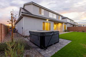 Back of house featuring a fenced backyard, a patio, stucco siding, and a hot tub