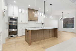 Kitchen featuring white cabinetry, glass insert cabinets, pendant lighting, brown cabinets, and light wood-style floors