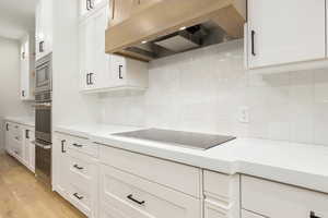 Kitchen featuring custom range hood, white cabinetry, light stone counters, and light wood finished floors