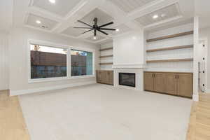 Unfurnished living room featuring a tile fireplace, coffered ceiling, light wood-style flooring, ceiling fan, and beam ceiling