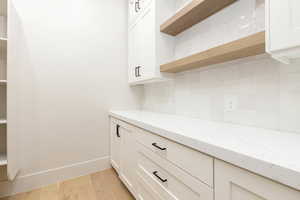 Bar area with light stone countertops, open shelves, backsplash, and white cabinets
