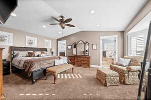 Carpeted bedroom with vaulted ceiling, ensuite bath, recessed lighting, multiple windows, and ceiling fan