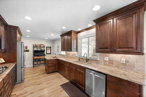 Kitchen with stainless steel appliances, light stone countertops, light wood-type flooring, decorative backsplash, and crown molding