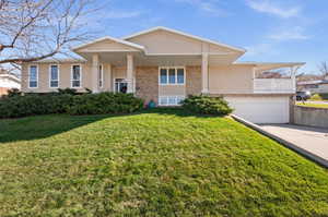 View of front of house with brick siding, concrete driveway, a front lawn, a garage, and a balcony