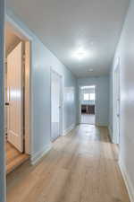 Corridor with a textured ceiling and light wood finished floors