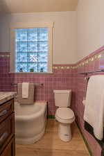 Full bath featuring a garden tub, wainscoting, vanity, light wood-style flooring, and tile walls