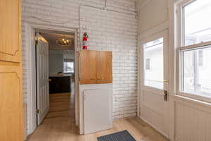 Doorway to outside featuring brick wall, wood finished floors, and a chandelier