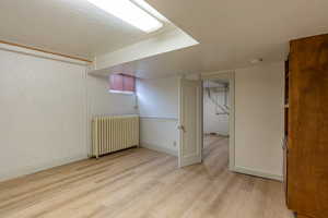 Finished below grade area with radiator, light wood-style floors, and brick wall