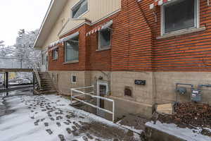 Snow covered property with stairway and brick siding