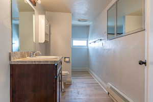 Half bathroom featuring a textured ceiling, a baseboard radiator, light wood-style flooring, vanity, and a textured wall