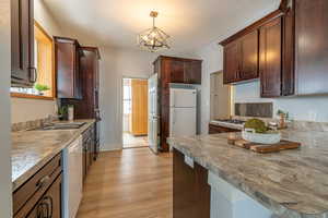 Kitchen with white appliances, decorative light fixtures, light wood-type flooring, a chandelier, and a peninsula