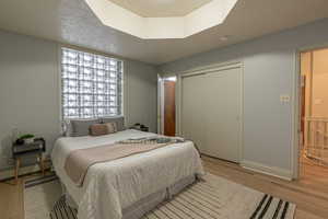 Bedroom featuring a closet, light wood finished floors, a textured ceiling, and a baseboard radiator