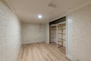 Unfurnished bedroom with brick wall, light wood-style floors, a closet, and concrete block wall