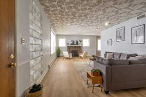 Living area featuring light wood-style floors, a baseboard radiator, and a brick fireplace
