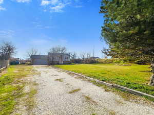 View of front of property featuring a front lawn, gravel driveway, an attached garage, and stone siding
