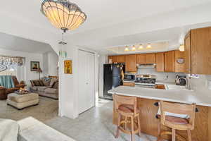 Kitchen featuring light countertops, a breakfast bar, stainless steel appliances, a raised ceiling, and light colored carpet
