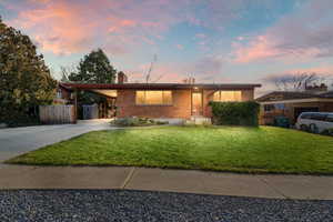 View of front of home featuring brick siding, concrete driveway, a chimney, a front yard, and a carport
