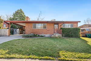 Ranch-style house with brick siding, an attached carport, a chimney, and driveway