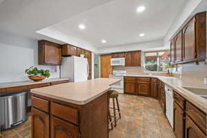 Kitchen featuring white appliances, a breakfast bar, light countertops, recessed lighting, and stone finish flooring