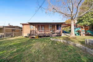 Rear view of property featuring a wooden deck, a playground, brick siding, and a fenced backyard
