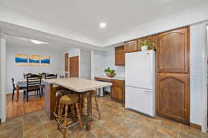 Kitchen with freestanding refrigerator, brown cabinets, light countertops, a kitchen bar, and stone finish floors
