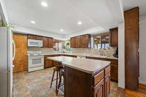 Kitchen featuring a breakfast bar, white appliances, stone finish floors, light countertops, and a center island