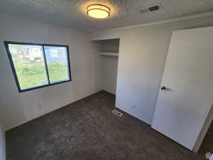 Unfurnished bedroom featuring dark carpet, a textured ceiling, and a closet