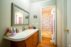 Bathroom with vanity, wood finished floors, shower / bathtub combination with curtain, and ornamental molding