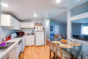 Kitchen with light countertops, white cabinets, white appliances, light wood-style flooring, and vaulted ceiling