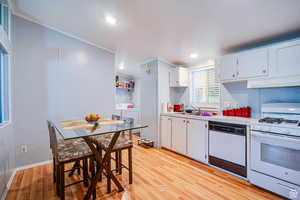 Kitchen with white appliances, white cabinetry, light countertops, light wood-style floors, and crown molding