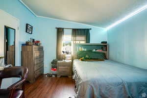 Bedroom featuring dark wood-style flooring, lofted ceiling, ornamental molding, and a textured ceiling