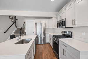 Kitchen featuring stainless steel appliances, a kitchen island with sink, wood tiled floors, white cabinetry, and light stone counters