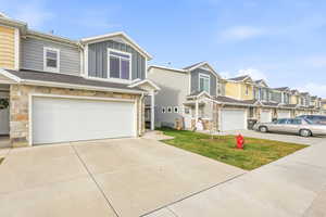 View of front of property featuring a residential view, an attached garage, concrete driveway, and stone siding