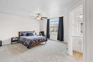 Bedroom with light colored carpet, connected bathroom, and a ceiling fan