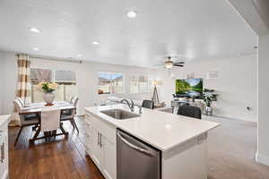 Kitchen with open floor plan, stainless steel dishwasher, white cabinets, a textured ceiling, and a center island with sink
