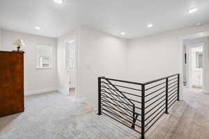Hallway with an upstairs landing, light colored carpet, and recessed lighting