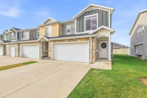 View of front of property featuring stone siding, board and batten siding, a garage, concrete driveway, and a front yard