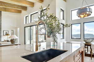 Kitchen with light stone countertops, a high ceiling, beamed ceiling, and healthy amount of natural light
